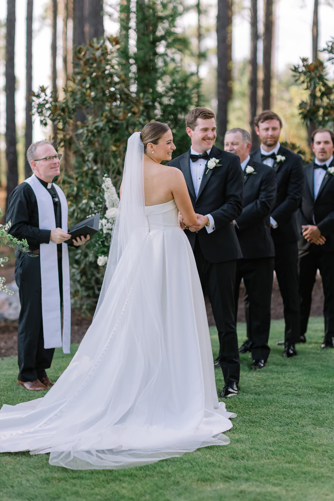 Brent, in black clerical attire with a white stole, officiating an outdoor wedding ceremony